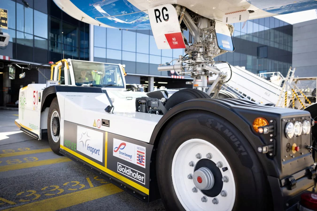 EcoTow21 Schlepper von Goldhofer mit Blick auf Vorderachse und Luftfahrzeugfahrwerk am Flughafen, Fraport-Logo und Strom bewegt Markenaufkleber sichtbar