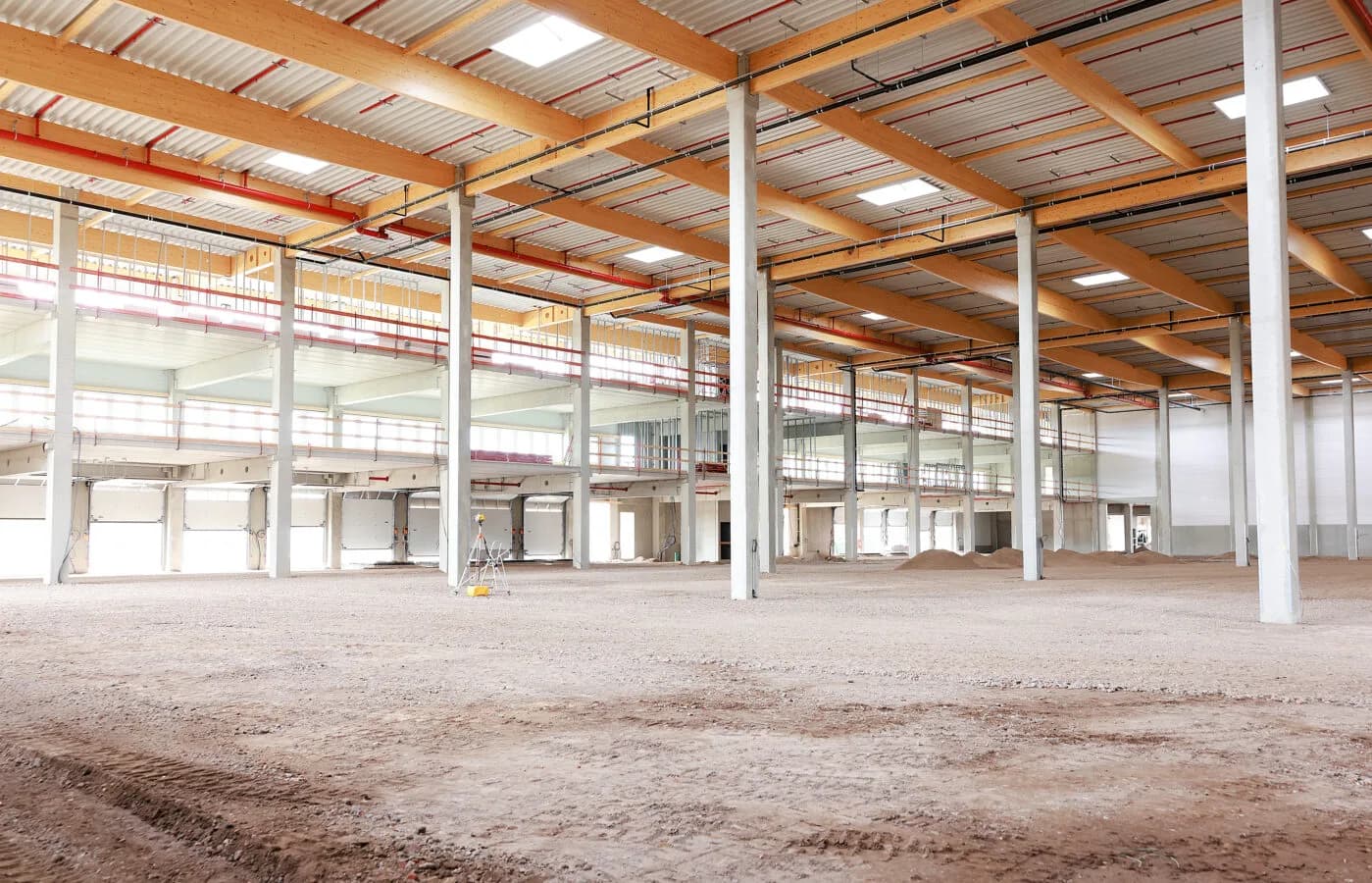Große Logistikhalle im Ausbau mit Stahlbetonstützen, Holzträgern, offenen Versandtoren und Bodenvorbereitung für LogiSpace Taubengrund