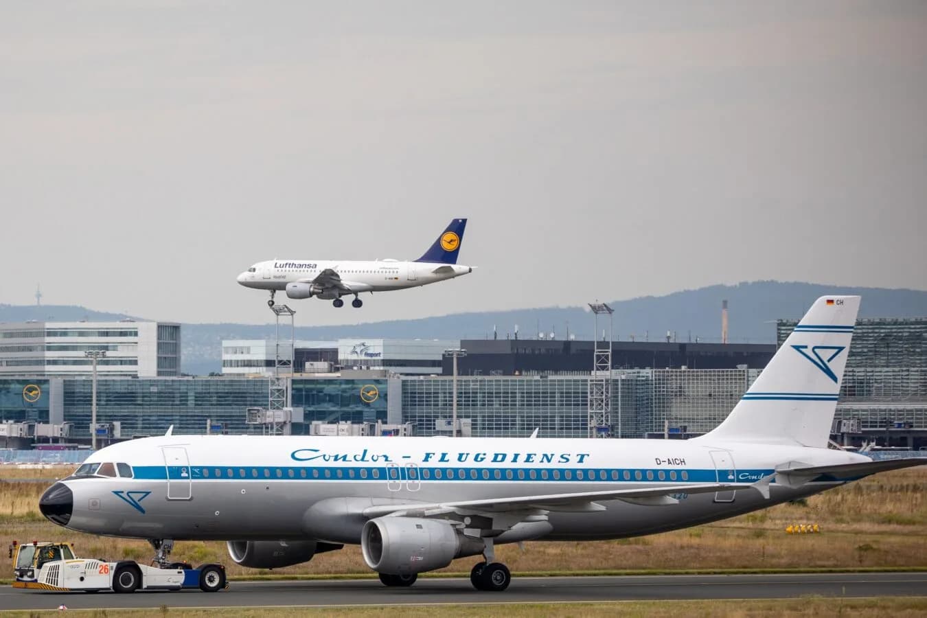 Condor Flugzeug im Retro-Design beim Schieben am Rollfeld vor Terminalgebäuden am Flughafen Frankfurt, im Hintergrund Lufthansa-Maschine im Landeanflug