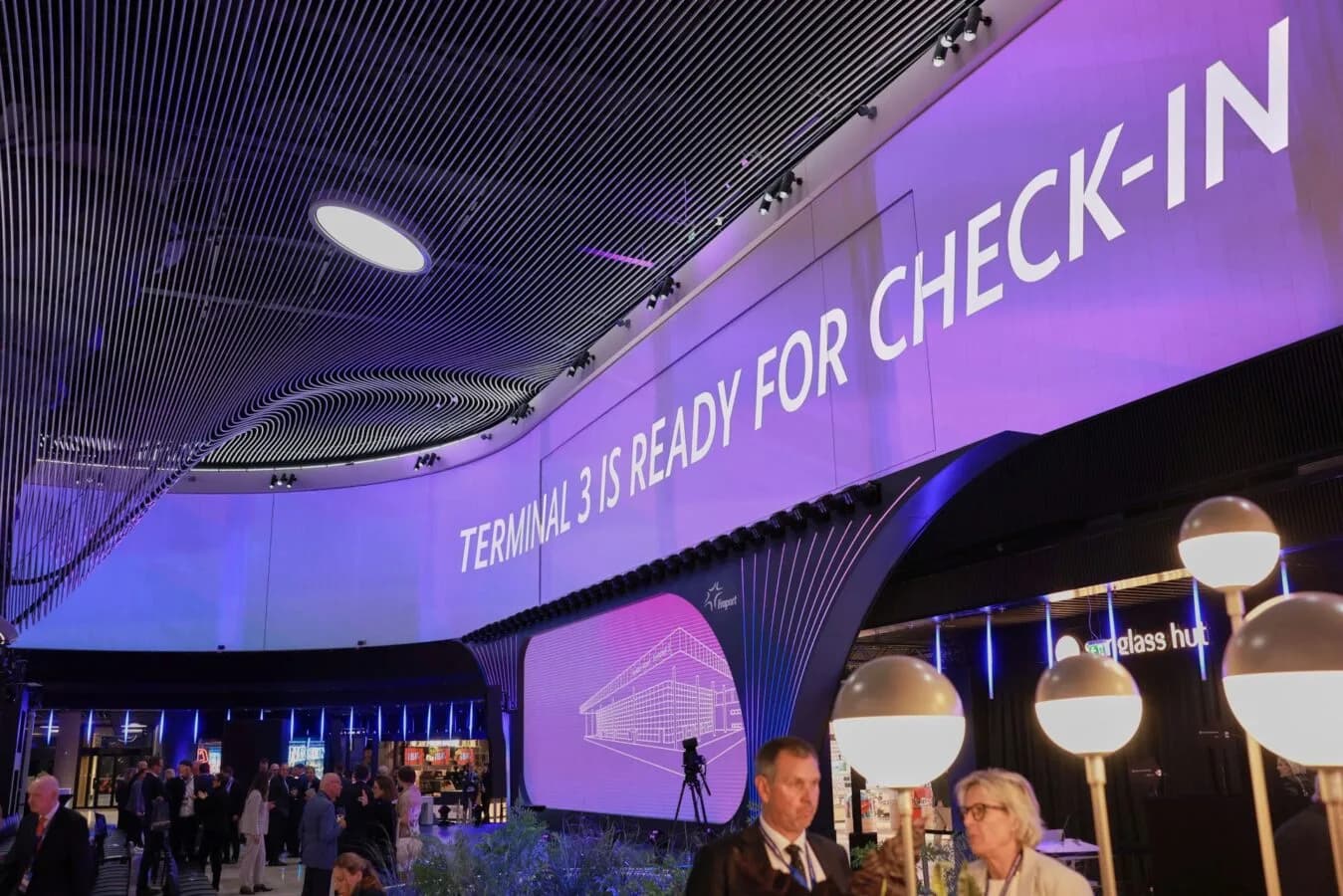 Flughafenterminal mit lila Beleuchtung und großer Projektion Terminal 3 is ready for check-in, Reisende und Informationsdisplay