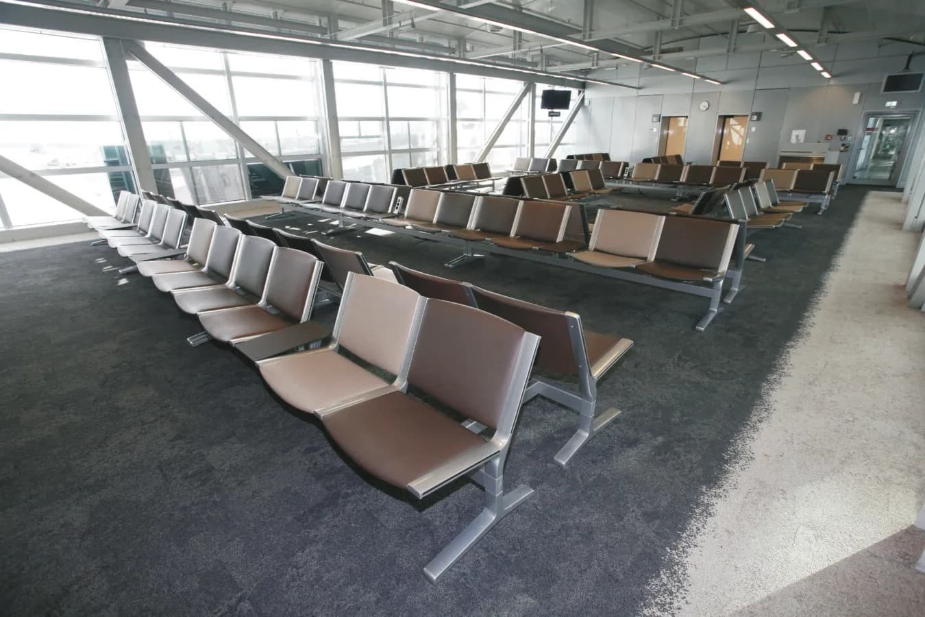 Leerer Gate-Wartebereich im Flughafen mit Reihen von metallischen Sitzbänken und braunen Polstersitzen vor großen Fensterfronten (c) Flughafen Frankfurt