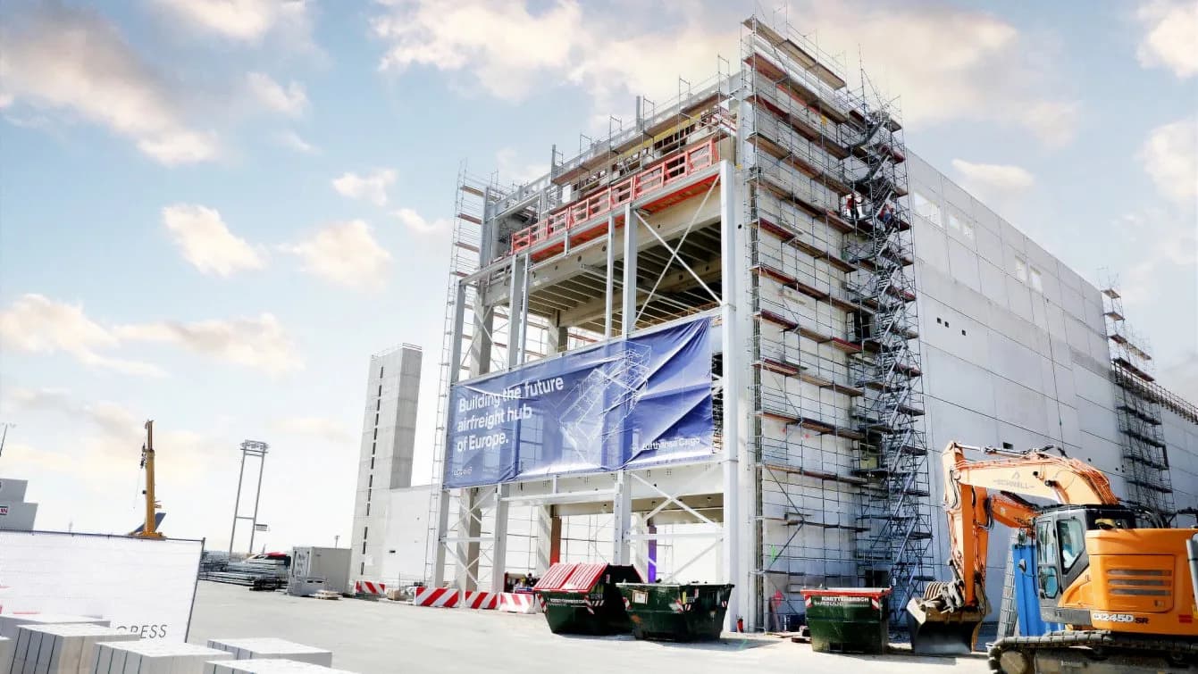 Lufthansa Cargo Center Evolution Baustelle mit Stahlkonstruktion, Gerüsten, Planenbanner und Bagger vor Frachtzentrumfassade