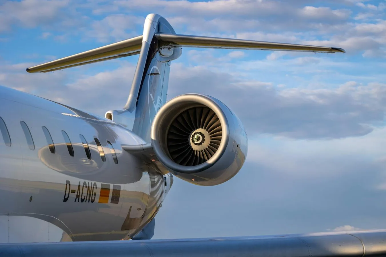 Triebwerk eines Regionaljets am Heck, glänzende Flugzeugrümpfe und Seitenleitwerk vor blauem Himmel