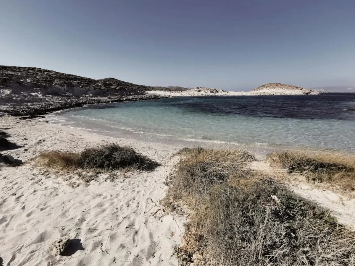 Sandstrand mit Dünenvegetation und türkisblauem Wasser einer abgelegenen Bucht auf griechischer Insel, klarer Himmel, ruhige Küstenszene ideal für Eurowings Aegean ParkSleepFly Reisen
