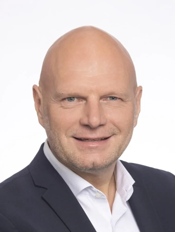 Geschäftsporträt eines lächelnden Mannes in Anzug und weißem Hemd vor hellem Hintergrund