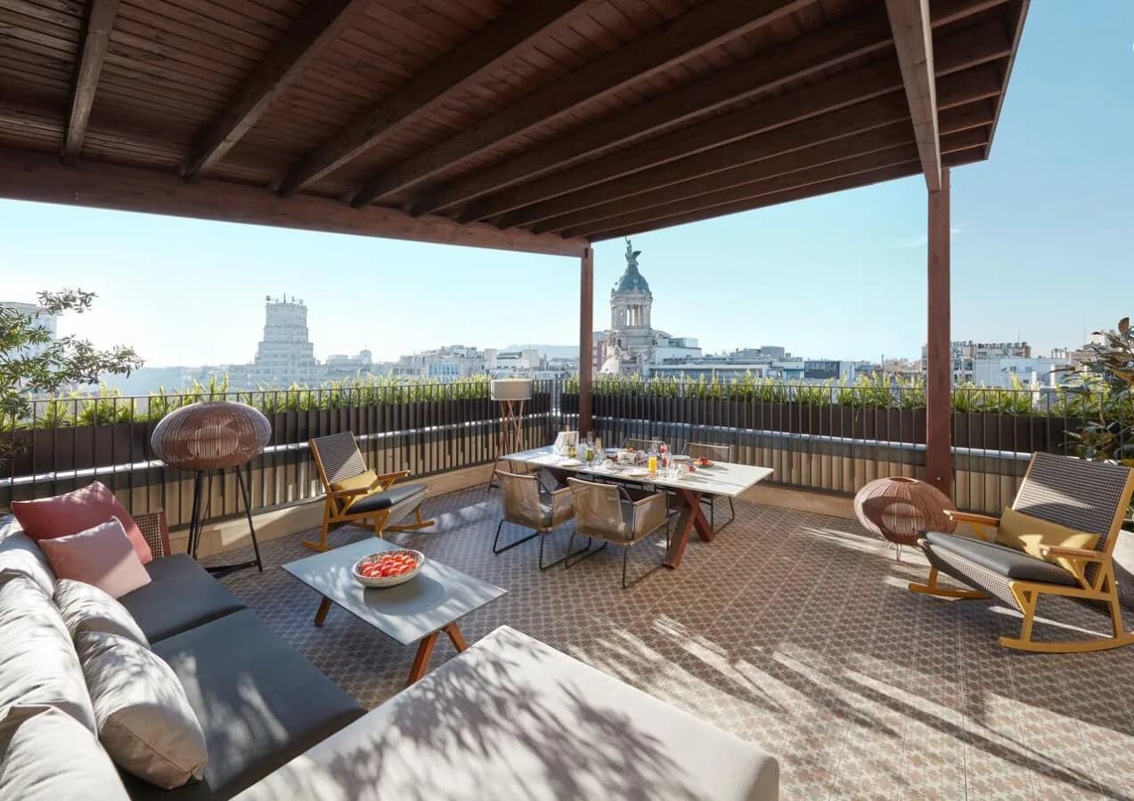Penthouse-Suite Terrasse im Mandarin Oriental Barcelona mit überdachtem Lounge- und Essbereich, gemütlichen Sitzmöbeln und Blick auf die Stadt und historische Türme