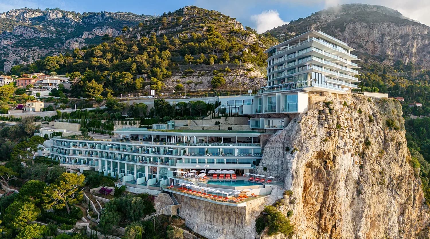 Maybourne Riviera Cap Martin Hotel an steiler Felsküste mit Terrassenpools, Sonnenliegen und Glasbalkonen vor mediterranen Pinienhängen in Cap-Martin, Côte d’Azur, Frankreich