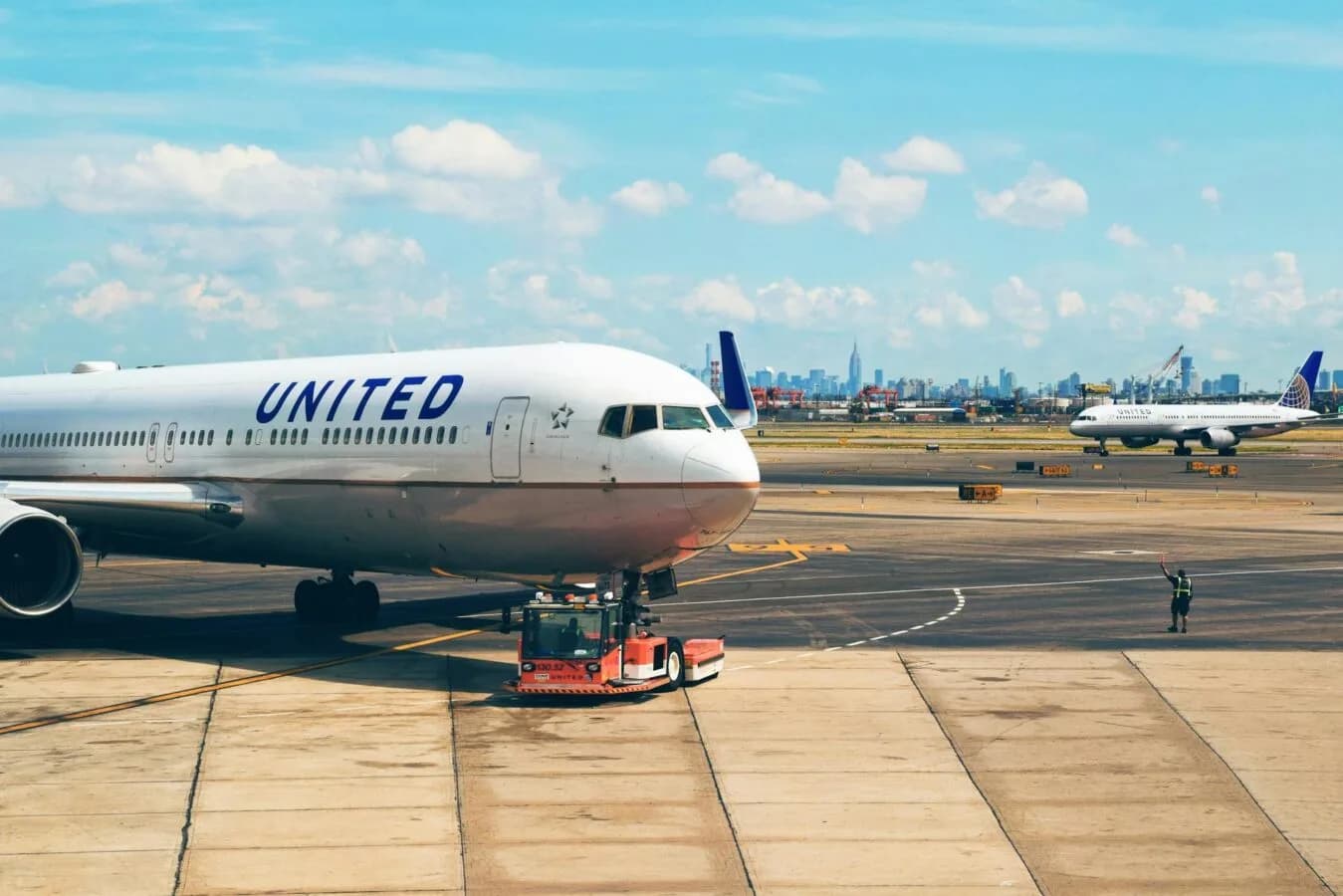 United Airlines Flugzeug am Gate mit Bodenfahrzeug und Mitarbeiter auf dem Vorfeld, weiteres United-Flugzeug rollt im Hintergrund