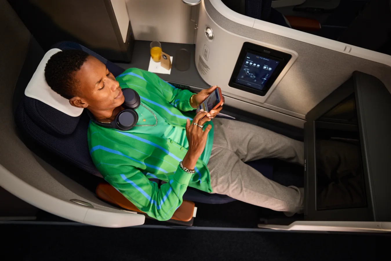 Passagier entspannt in Lufthansa Business Class Suite, flach gestellter Sitz mit Kopfstütze, Kopfhörer, Tablet-Bedienfeld, Getränk und Smartphone nutzen