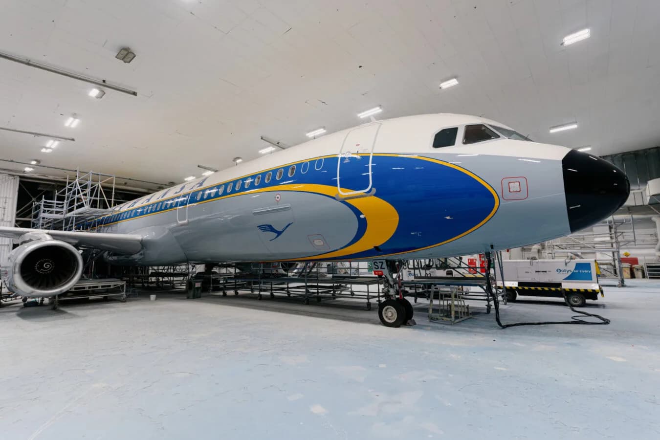 Lufthansa A321 Passagierflugzeug im Hangar mit blau-gelber Sonderlackierung und freiem Blick auf Rumpf, Triebwerk und Bugfahrwerk