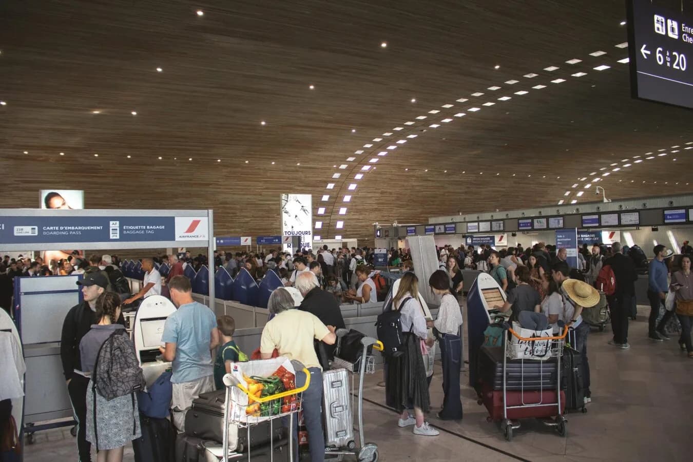 Voller Flughafen-Check-in Bereich mit Warteschlangen, Gepäckwagen und Passagieren vor Abfertigungsschaltern