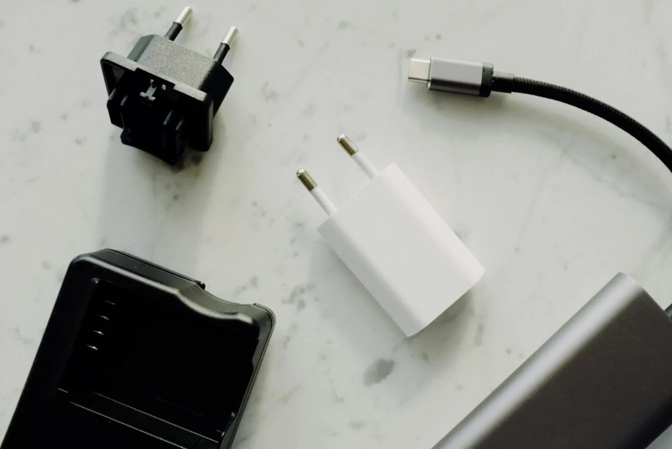 Verschiedene Ladegeräte und Kabel auf hellem Untergrund, Powerbank und Steckadapter im Kontext neuer Lufthansa-Regelungen