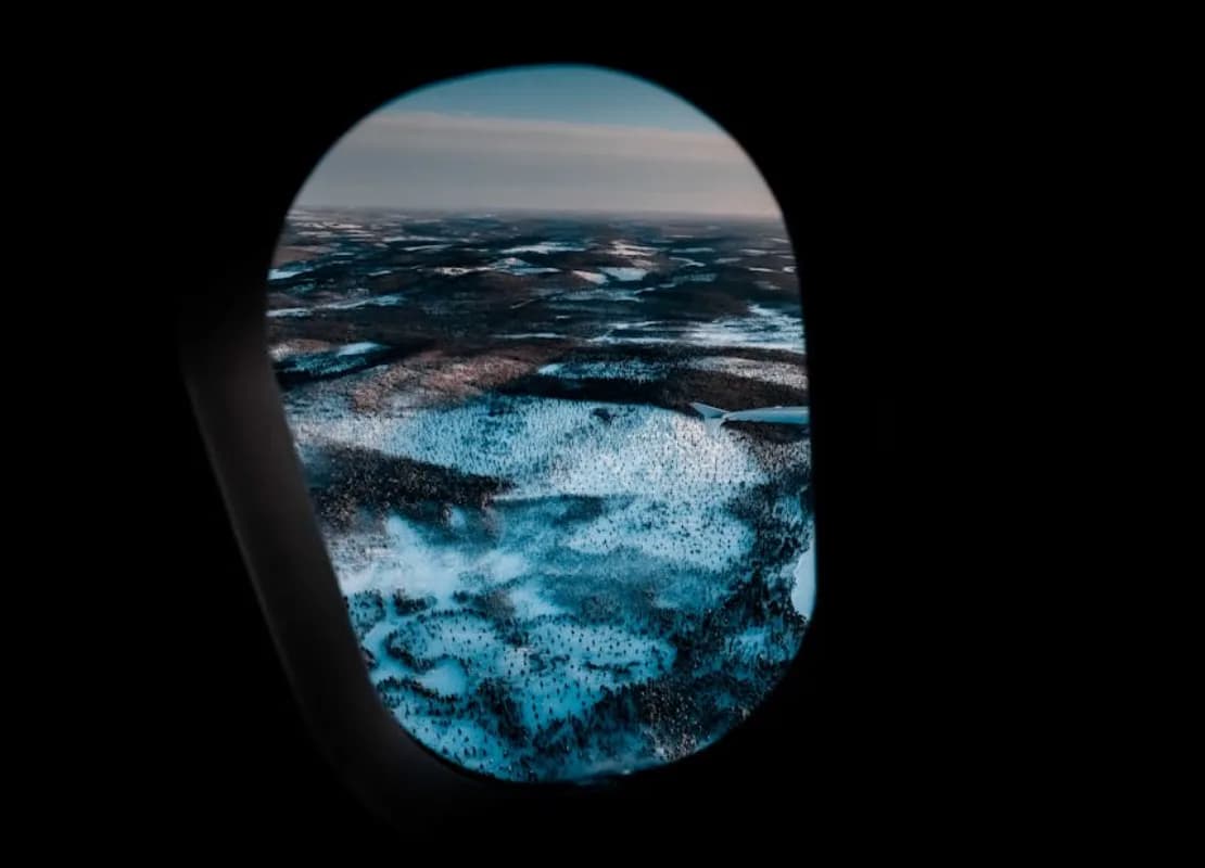 Blick aus einem Flugzeugfenster auf verschneite Winterlandschaft und Hügel bei Flug über Deutschland, Winterflugplan Flughafen Frankfurt
