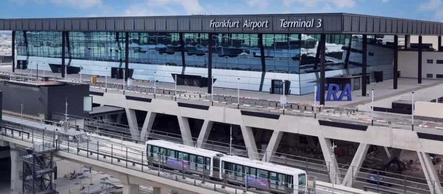 Blick auf das moderne Terminal 3 des Flughafens Frankfurt mit glasfassade, Vorfahrtbereich und fahrender automatischer Skyline-Bahn