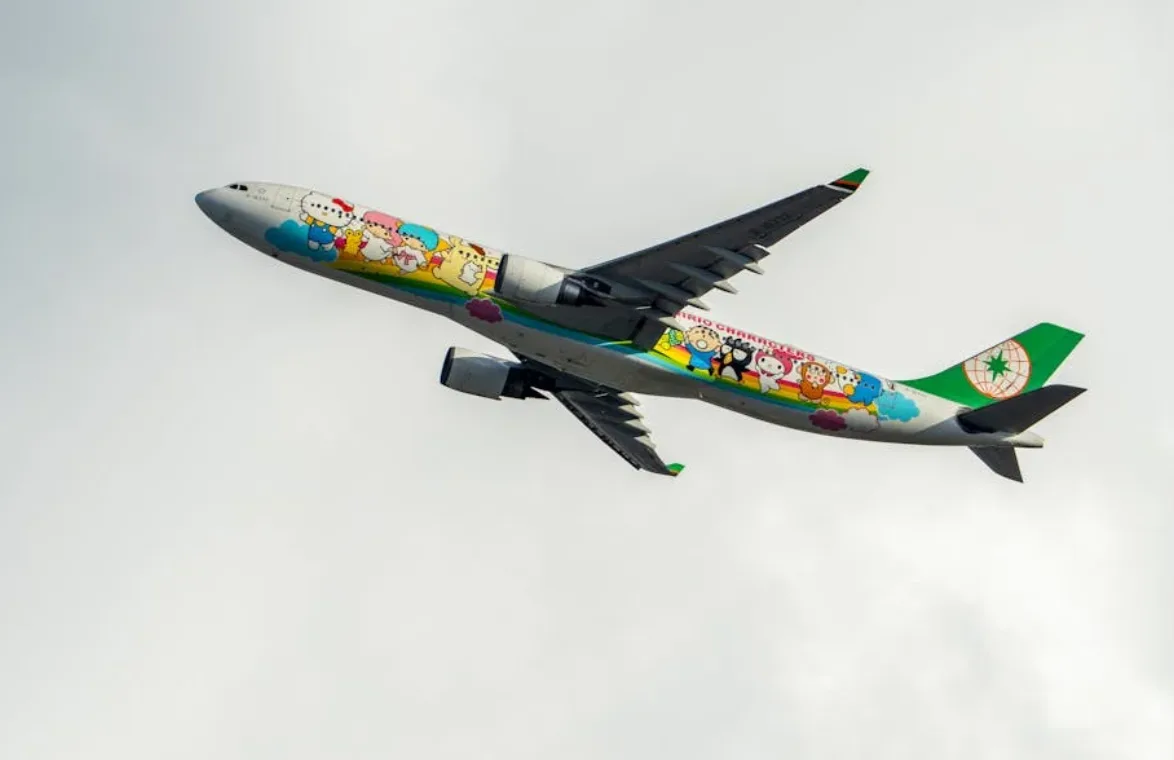 Passagierflugzeug mit buntem Cartoon-Design und grüner Leitwerk-Markierung fliegend vor hellem Himmel
