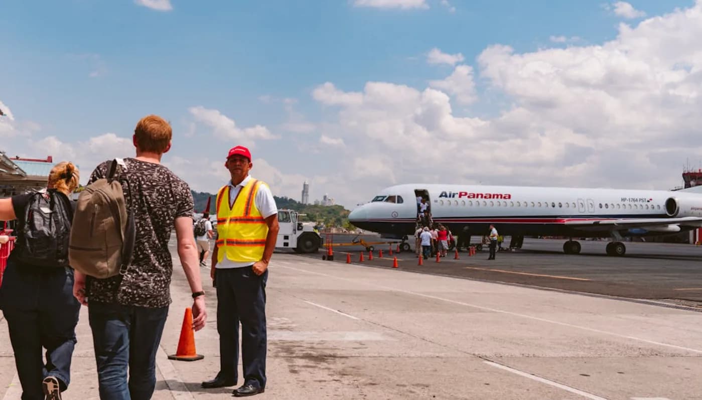 Passagiere steigen über das Vorfeld in ein Air Panama Flugzeug ein, Bodenpersonal mit Warnweste leitet den Weg bei sonnigem Himmel