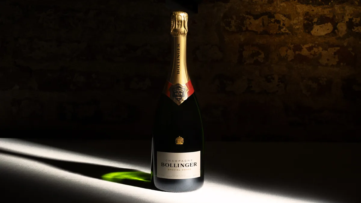 Flasche Bollinger Champagner auf beleuchteter Oberfläche vor dunkler Mauer, Nahaufnahme Produktpräsentation