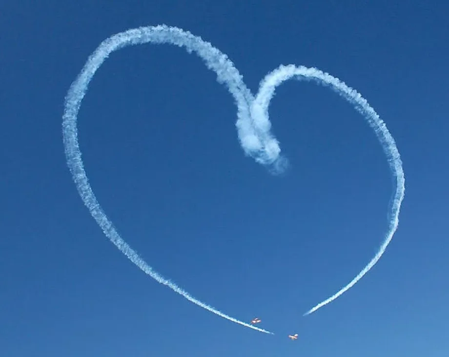 Zwei Kunstflugmaschinen zeichnen ein Herz aus Kondensstreifen vor blauem Himmel, Park Sleep Fly oneworld SAF Fonds Bezug