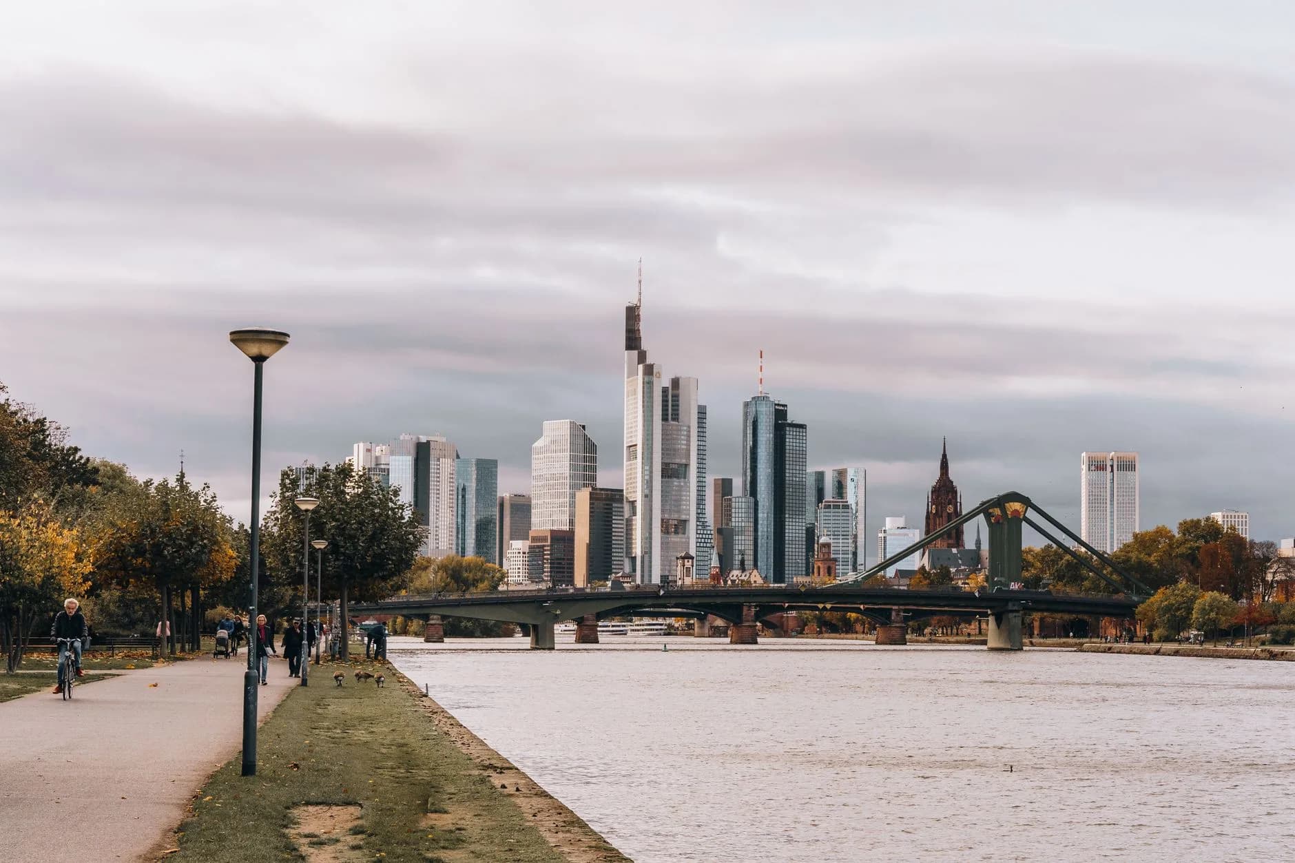Skyline von Frankfurt am Main mit Flößerbrücke, Flusspromenade und Spaziergängern im Herbst