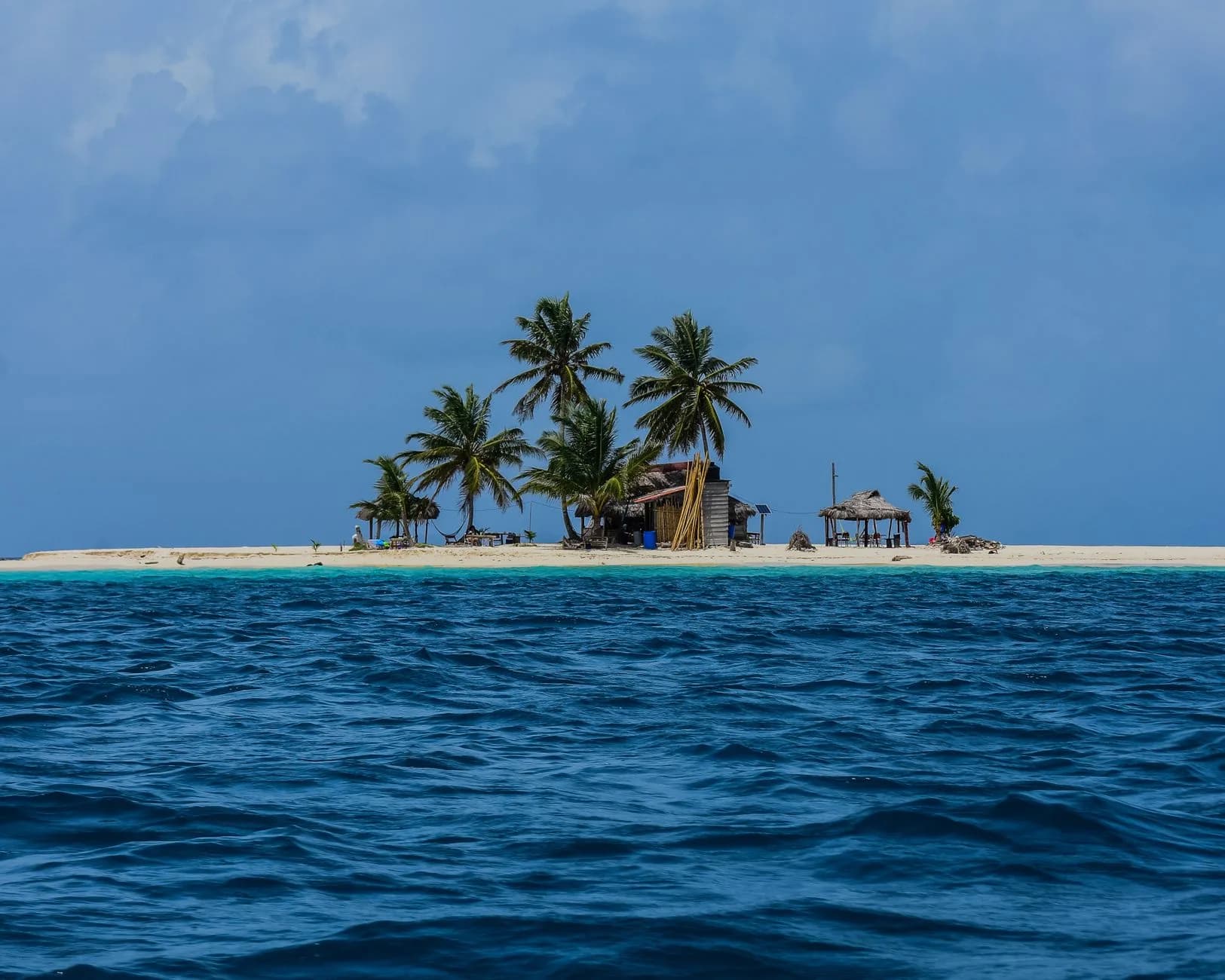 Kleine Sandinsel mit Palmen und einfachen Hütten, umgeben von türkisfarbenem und tiefblauem Meer