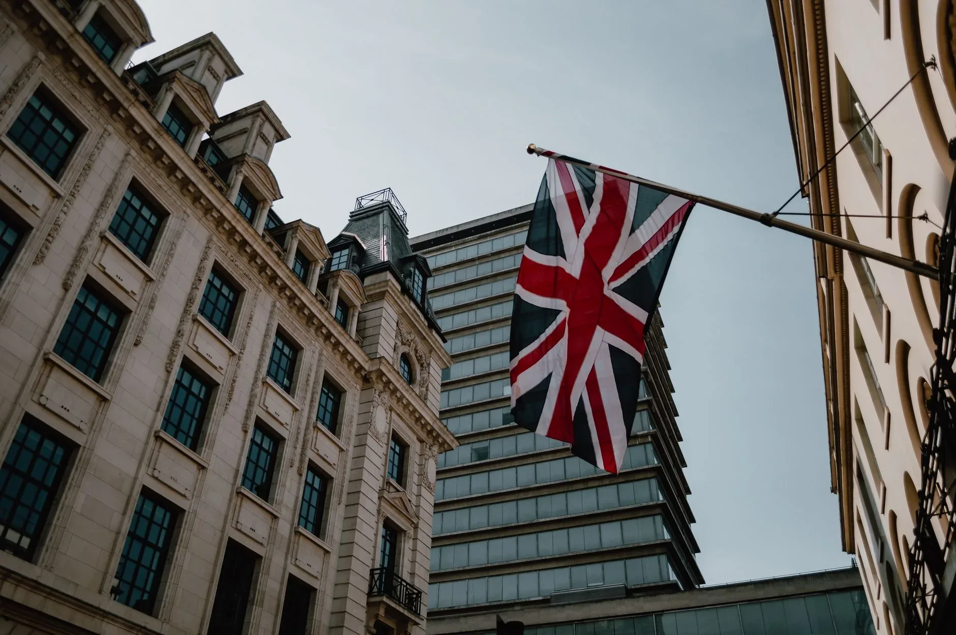 Union Jack hängt an einer Fahnenstange zwischen historischen Gebäuden und einem Hochhaus in einer britischen Innenstadt