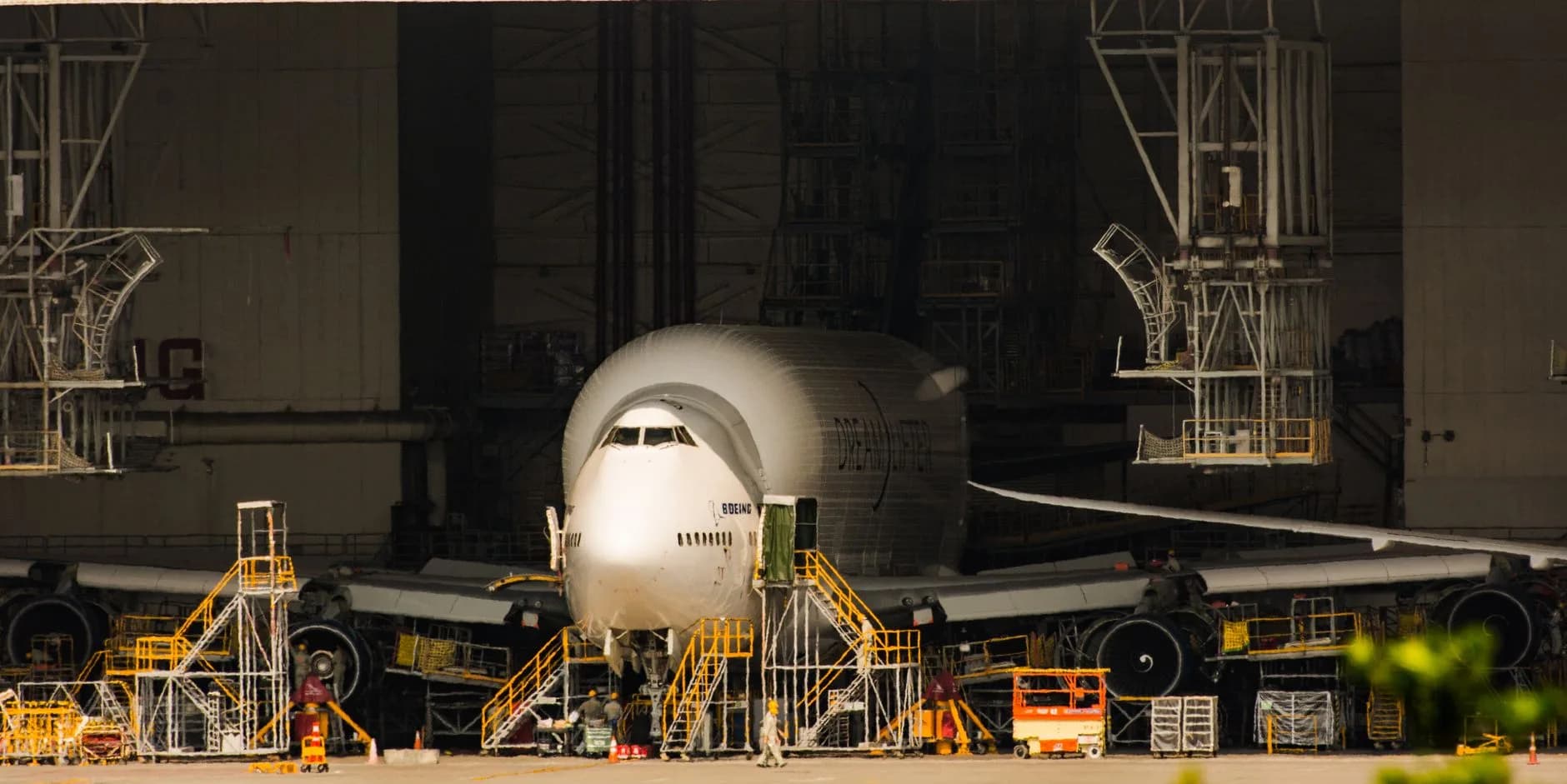 Boeing Dreamlifter mit bauchigem Rumpf steht vor einem Hangar, umgeben von Wartungsgerüsten und Bodenpersonal
