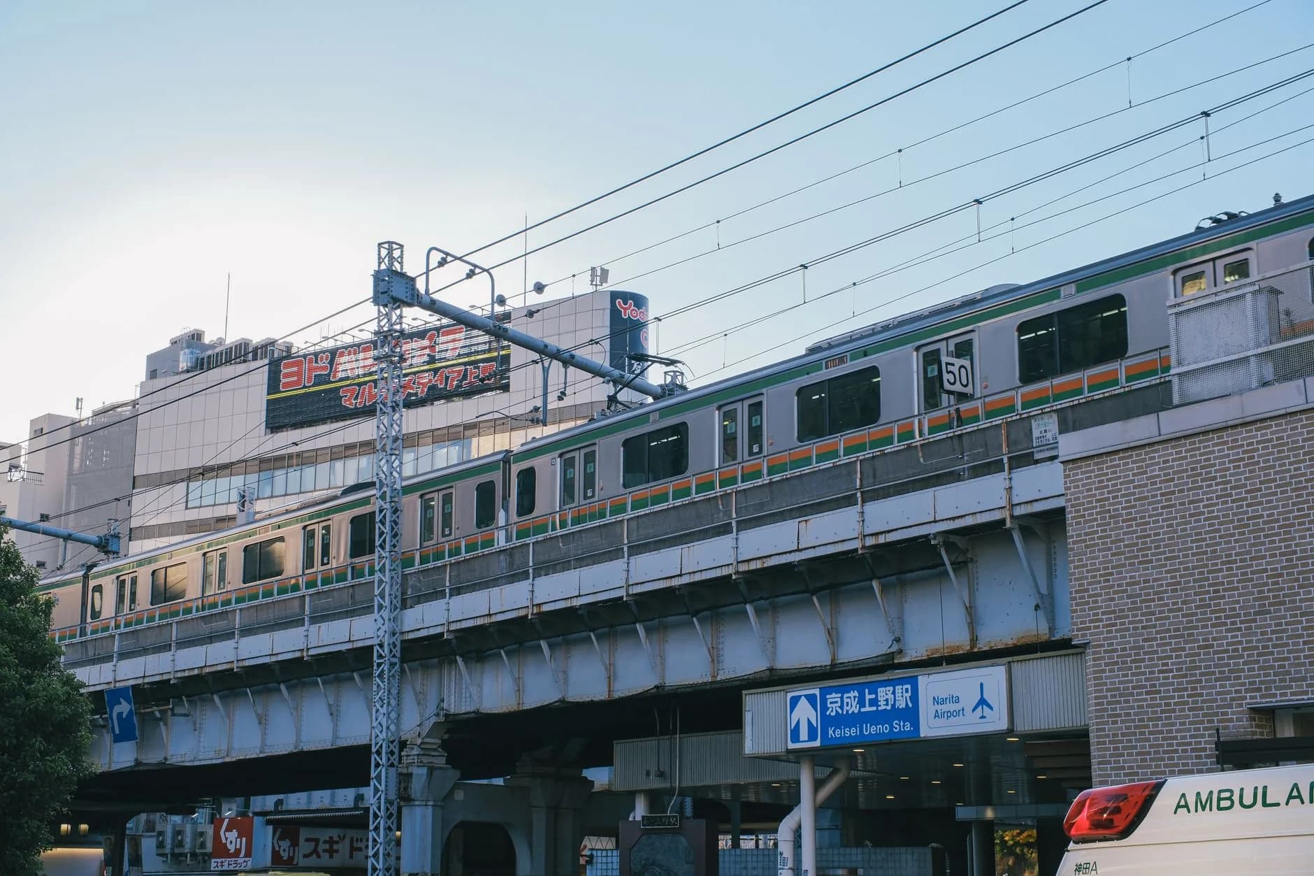 Zug auf Hochbahngleis über Straßenschild zum Keisei Ueno Bahnhof mit Richtung Narita Airport