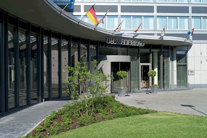 Eingangsbereich des NH Frankfurt Niederrad mit Drehflügeltür, Glasfassade, Flaggen und Vorgarten.