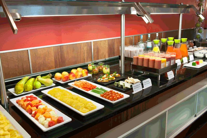 Frühstücksbuffet mit Obst, Gemüse, kleinen Gläsern und Karaffen mit Säften auf schwarzem Tresen.