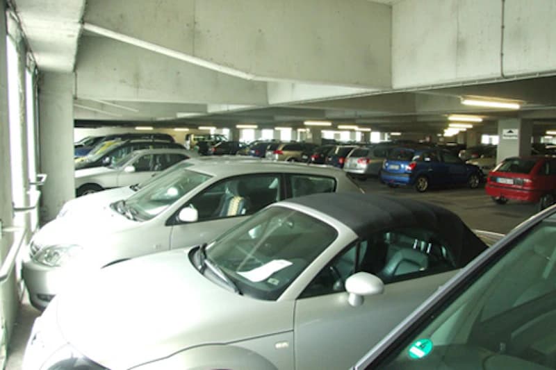 Parkdeck in einem Parkhaus mit geparkten Autos, Betonstützen und Deckenbeleuchtung.