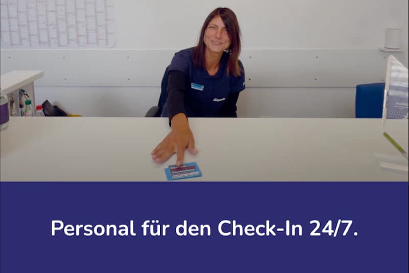 Mitarbeiterin hinter Empfangstresen reicht eine Karte, Airparks-Schriftzug auf ihrer Kleidung.