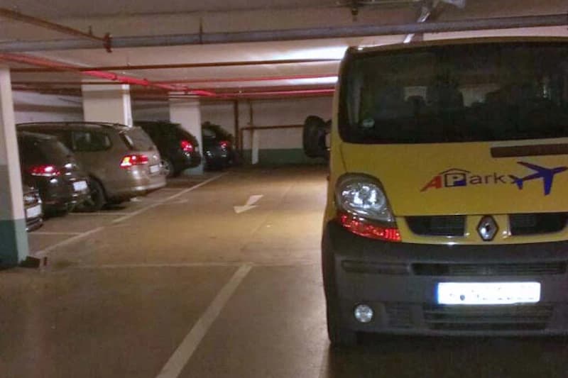 Tiefgarage mit mehreren geparkten Autos links und gelbem APark-Servicefahrzeug rechts im Vordergrund.