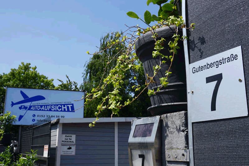 Einfahrt mit Sprechanlage und Hausnummer Gutenbergstraße 7, links Schild Auto-Aufsicht mit Flugzeuglogo und Telefonnummer.