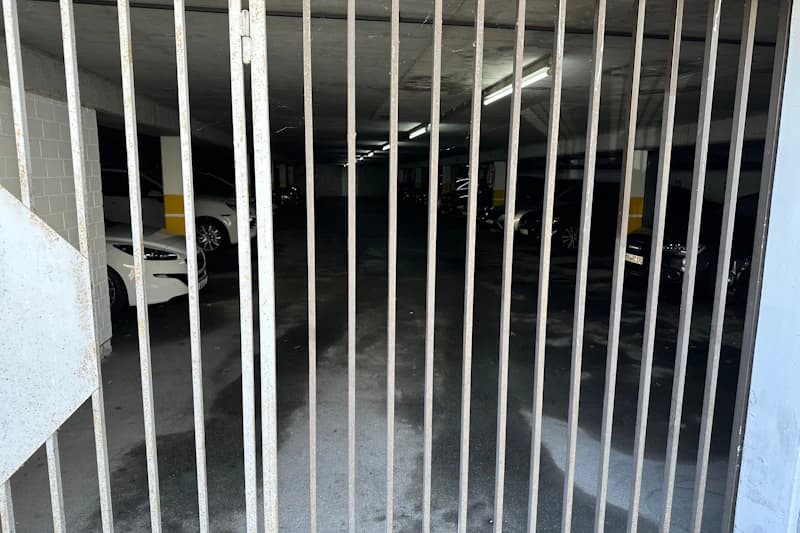 Metallgitter vor Eingang zu einer beleuchteten Tiefgarage mit geparkten Autos.