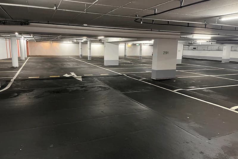 Leere, gut beleuchtete Tiefgarage mit markierten Stellplätzen, Pfeilmarkierung und Säule mit Nummer 291.