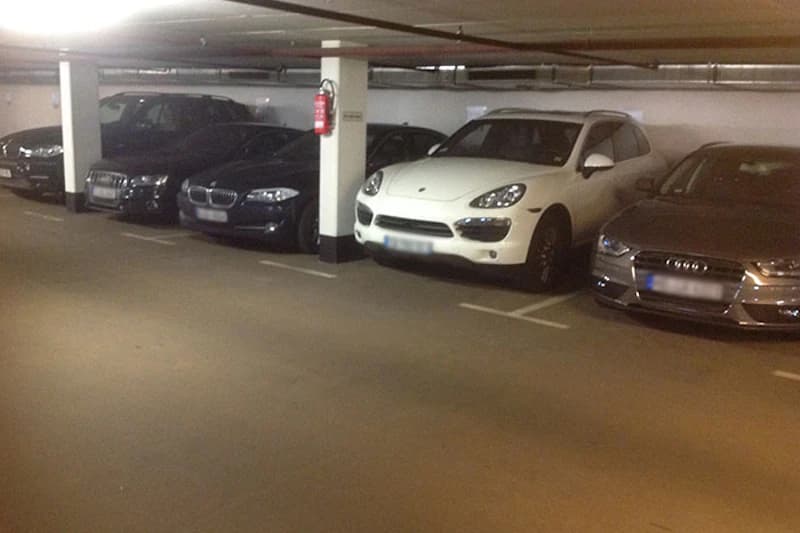 Tiefgarage mit mehreren geparkten Pkw, Stützsäulen und an einer Säule befestigtem Feuerlöscher.