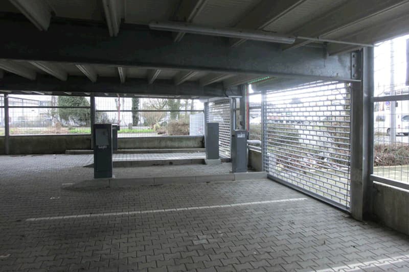 Überdachte Parkebene mit zwei Zahlstellenautomaten, markierten Stellplätzen und seitlichem Rollgitter im Parkhaus.