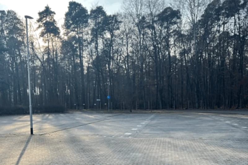Leerer gepflasterter Parkplatz mit Laterne und dichtem Baumbestand im Hintergrund am Flughafen Frankfurt.