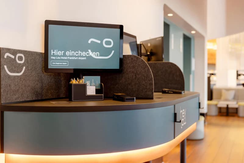 Rezeptionstheke mit Monitor Hier einchecken, Stifteköcher und graue Trennwände in der Hotel-Lobby.