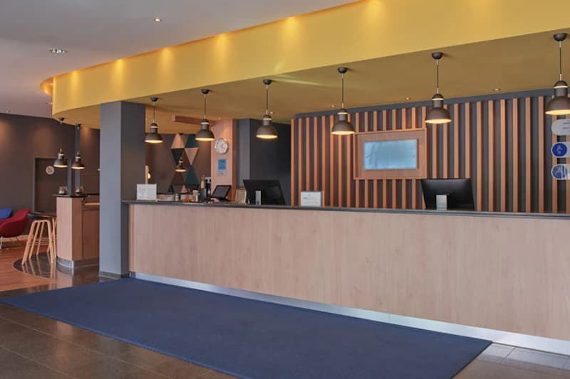 Hotelrezeption mit langem Empfangstresen, mehreren Hängelampen und blauem Läuferteppich.