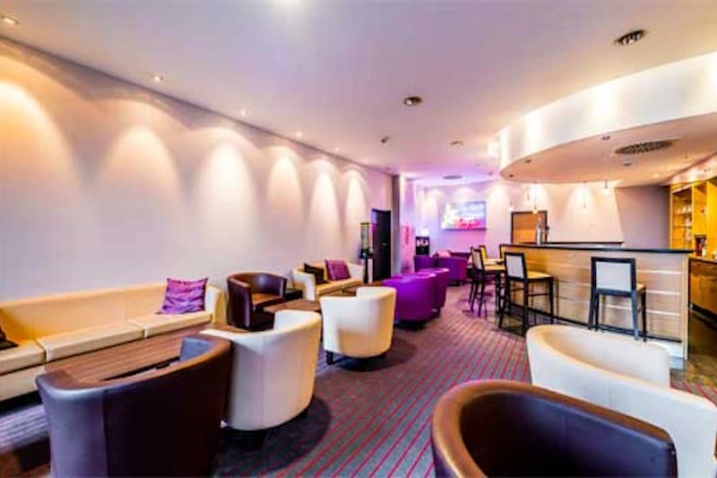 Hotel-Aufenthaltsbereich mit Sofas, runden Sesseln, Bartheke und indirekter Deckenbeleuchtung.
