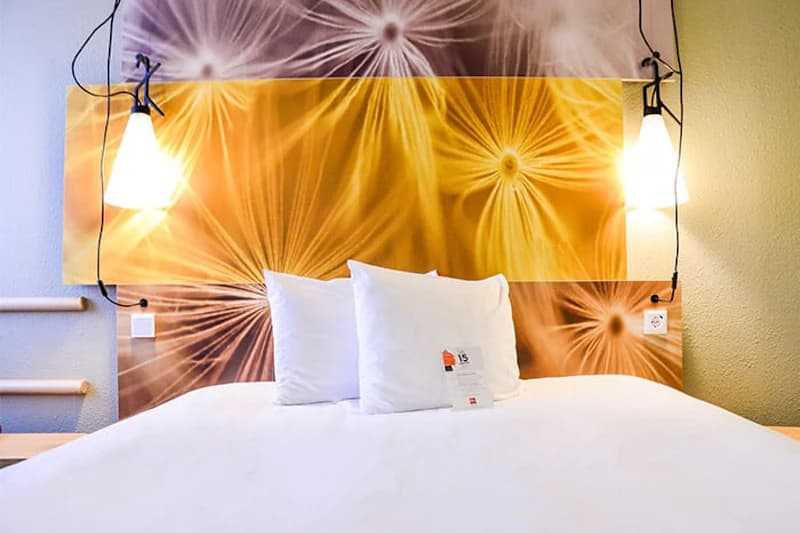 Doppelbett mit drei Kissen, dekorativem Kopfteil mit sternförmigem Blumenmuster und zwei hängenden Nachttischlampen.
