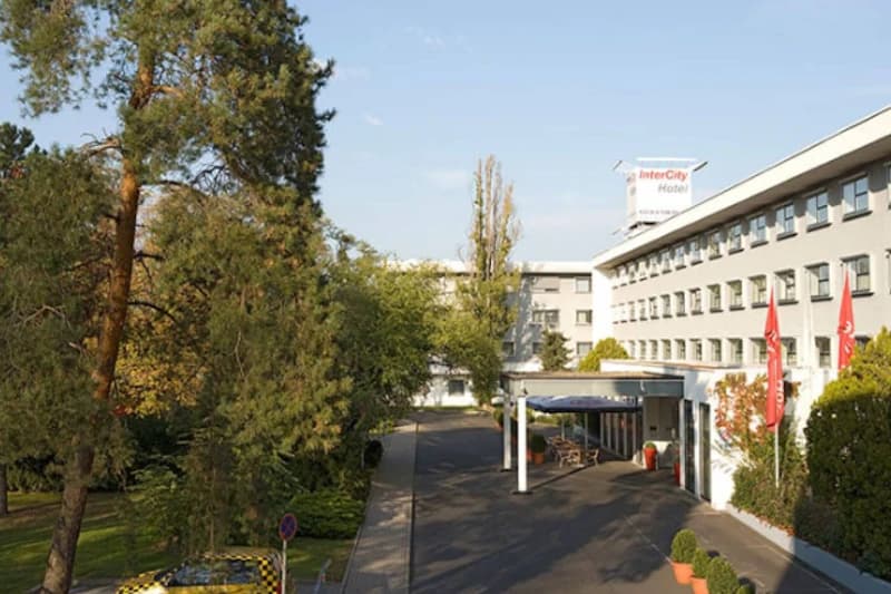 Mehrstöckiges graues Hotelgebäude mit Eingangsüberdachung, Einfahrt, Bäumen und Dachschild IntercityHotel.