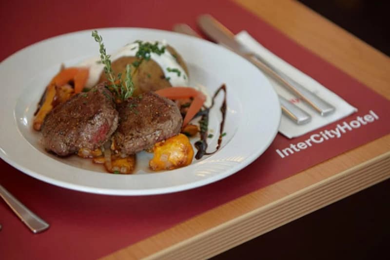 Zwei Rinderfiletmedaillons mit Kartoffel, Gemüse und Sauce auf Teller, Besteck auf InterCityHotel-Serviette.