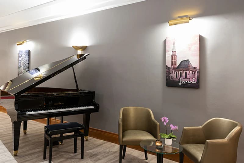 Schwarzer Flügel mit Hocker, zwei Sessel, Glastisch mit Orchidee und Wandbilder in einer Hotellobby.