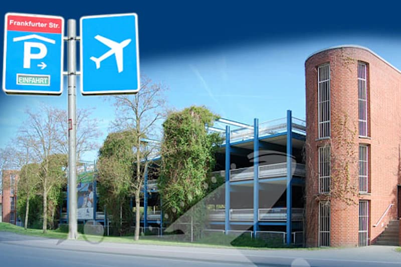 Mehrstöckiges Parkhaus mit rotem Backsteinturm und blauen Stahlträgern, Parksymbol und Flugzeugsymbol an der Straße.