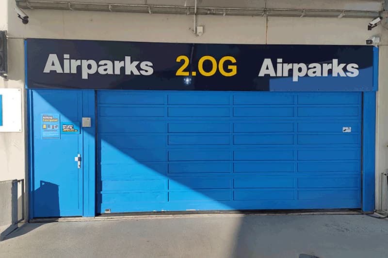 Blaues Rolltor mit Aufschrift Airparks 2.OG, kleine Tür links und Überwachungskamera an der Decke.