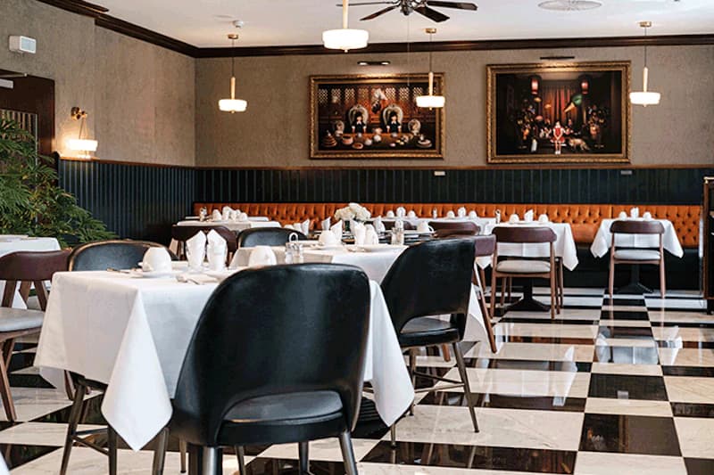 Restaurant mit schwarz-weiß kariertem Boden, gedeckten Tischen, schwarzen Stühlen und orangefarbener Polsterbank.