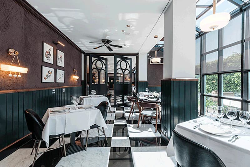 Elegantes Hotelrestaurant mit schwarz-weiss kariertem Boden, gedeckten Tischen und großen Fenstern.