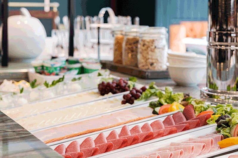 Aufgeschnittene Wurst- und Käsescheiben in Schalen, Trauben, Müsligläser und Schalen auf einem Frühstücksbuffet.